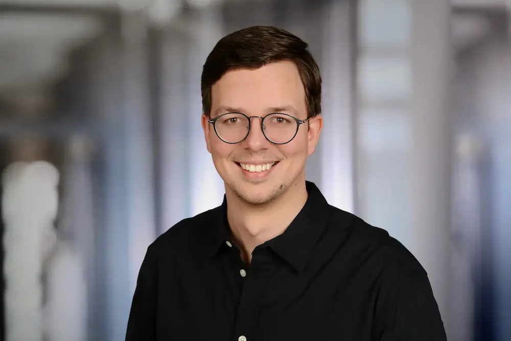 Portrait of Dmitry Dugarev wearing glasses in a black shirt and smiling