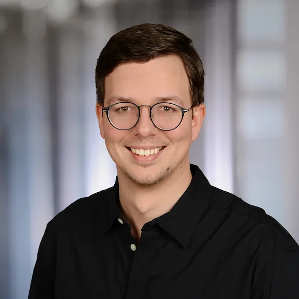 Portrait of Dmitry Dugarev wearing glasses in a black shirt and smiling